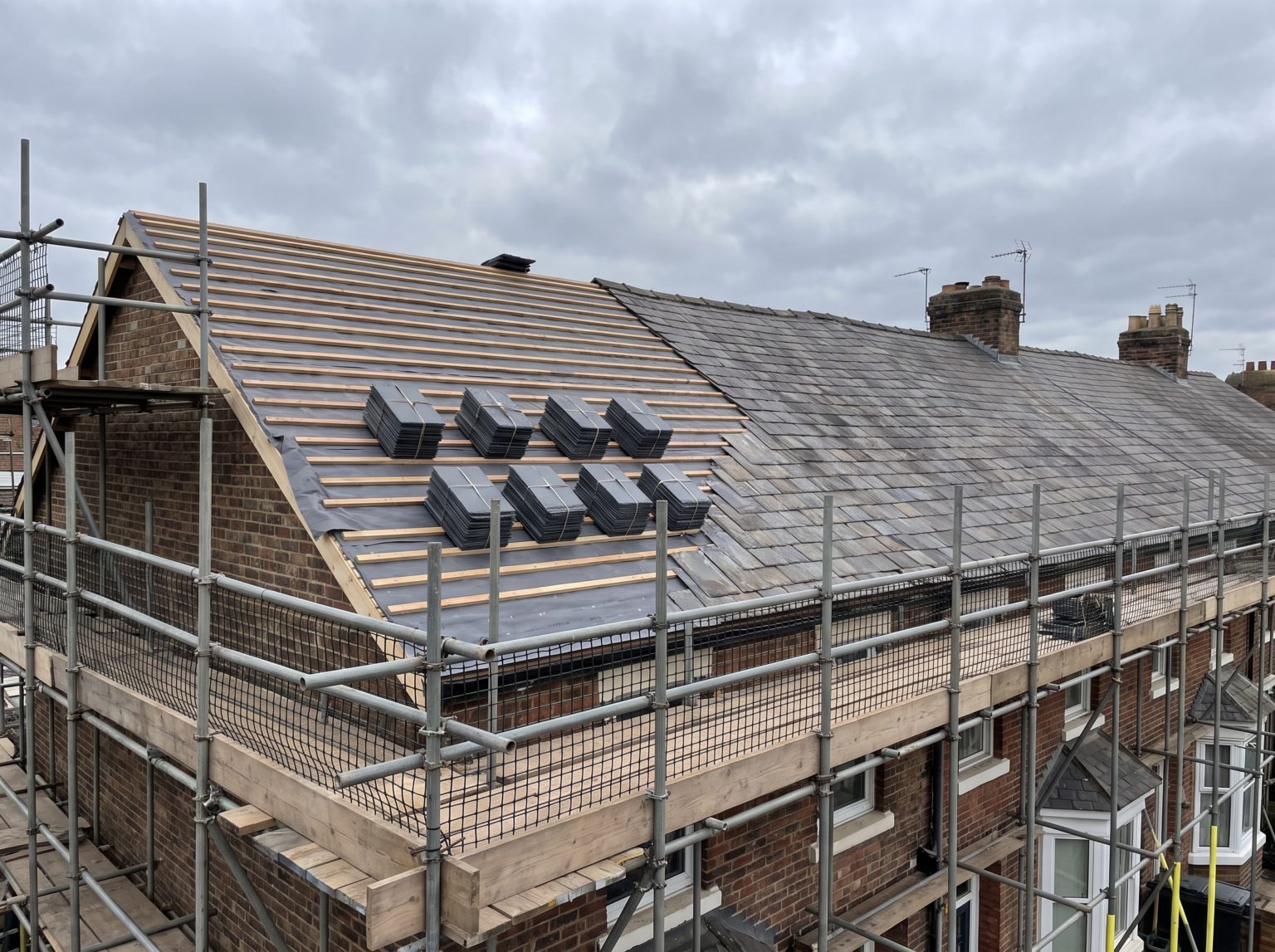 A pitched roof part-way through a strip and re-cover, battens and underlay exposed with scaffolding at the eaves
